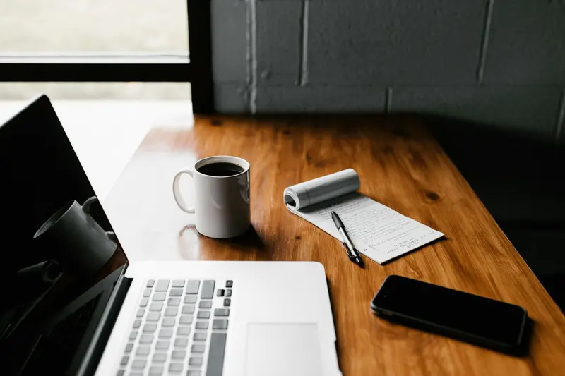 Warm wood desk with laptop, coffee, phone and notepad