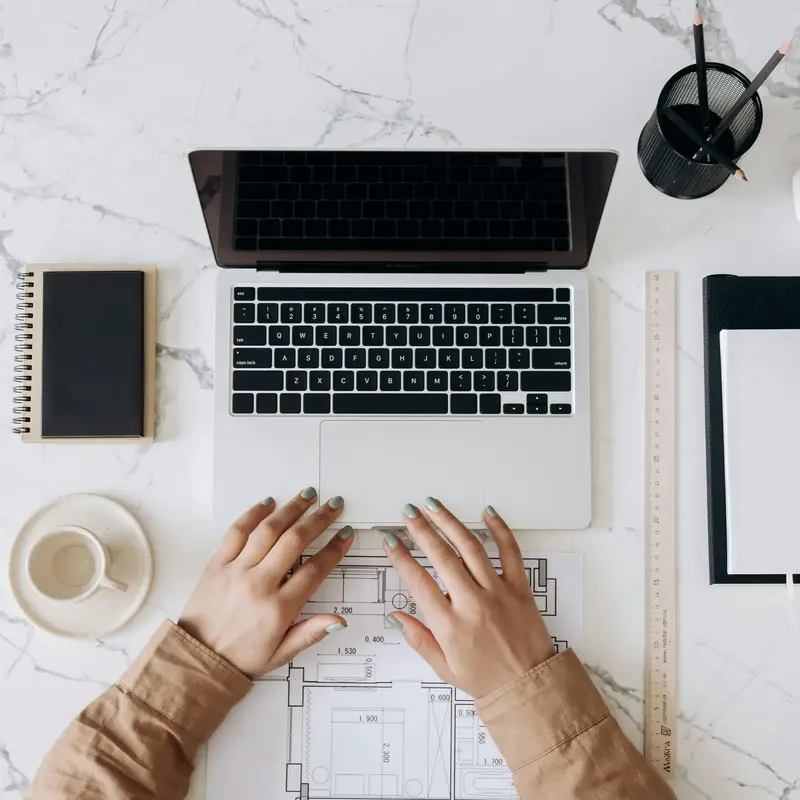 hands resting on a laptop keyboard surrounded by paperwork